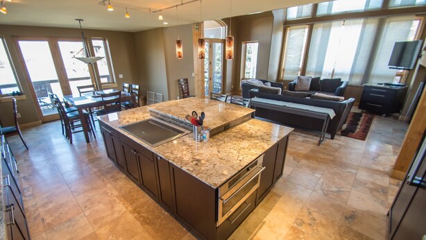 A spacious kitchen with a large island, dark cabinetry, and a dining area with chairs and a table.