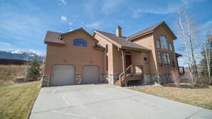 A two-story house with a stone foundation, a garage, and a mountain backdrop.