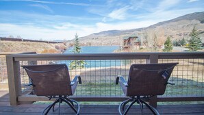 Two wicker chairs on a balcony overlooking a lake with a mountain backdrop.