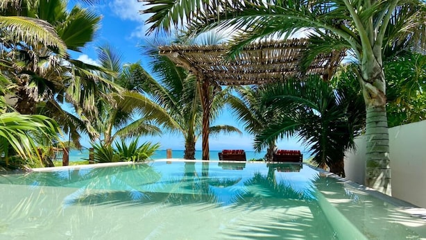An infinity pool with clear water, surrounded by palm trees and a thatched roof structure. - Casa Luna. Welcome Family To Enjoy A beautiful beach ! (Chelem)