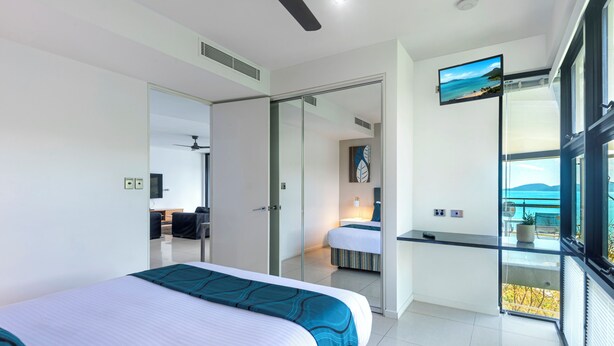 A modern hotel room with a bed, a desk, a TV, and a balcony with a view. - Edge Apartment 19, Seaview Apartment on Hamilton Island (Hamilton Island)
