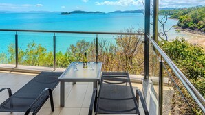 A balcony with a table and two chairs, overlooking a scenic view of a body of water and distant land. - Edge Apartment 19, Seaview Apartment on Hamilton Island (Hamilton Island)