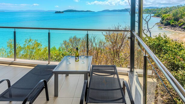 Varanda com mesa e duas cadeiras, com vista panorâmica para um corpo de água e terras distantes.