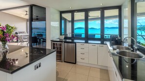 Uma cozinha moderna com uma ilha grande, armários brancos e vista para o mar.