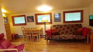 A living room with a wooden floor, a sofa with red cushions, a dining table with chairs, and a floor lamp. - Spacious and comfy, king bed, double futon sofa, kitchen, near Colgate, 7 Oaks (Hamilton)