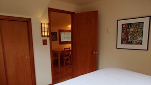 A bedroom with a large bed, wooden doors, a dining area with a table and chairs, and a framed artwork on the wall. - Spacious and comfy, king bed, double futon sofa, kitchen, near Colgate, 7 Oaks (Hamilton)