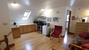 A compact living space with a kitchen, a red armchair, and a sofa with red cushions. - Spacious and comfy, king bed, double futon sofa, kitchen, near Colgate, 7 Oaks (Hamilton)