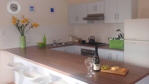 Une cuisine moderne avec un plan de travail en bois, des tabourets de bar blancs, une cuisinière à gaz et une bouteille verte posée sur le plan de travail.