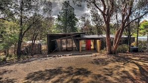 Une maison moderne dotée d’une grande porte vitrée, entourée d’arbres et bordée d’une allée en gravier.