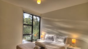 Une chambre à coucher avec un grand lit, deux lampes de chevet et une vue sur les arbres par la fenêtre.