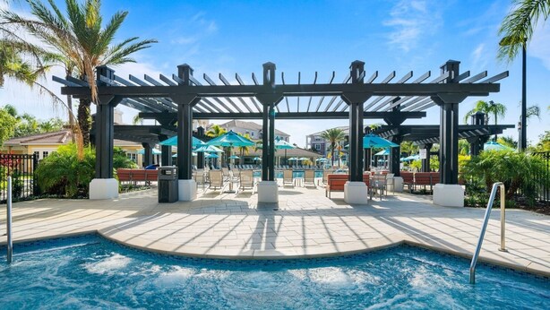 A pool area with a pergola, lounge chairs, and umbrellas.