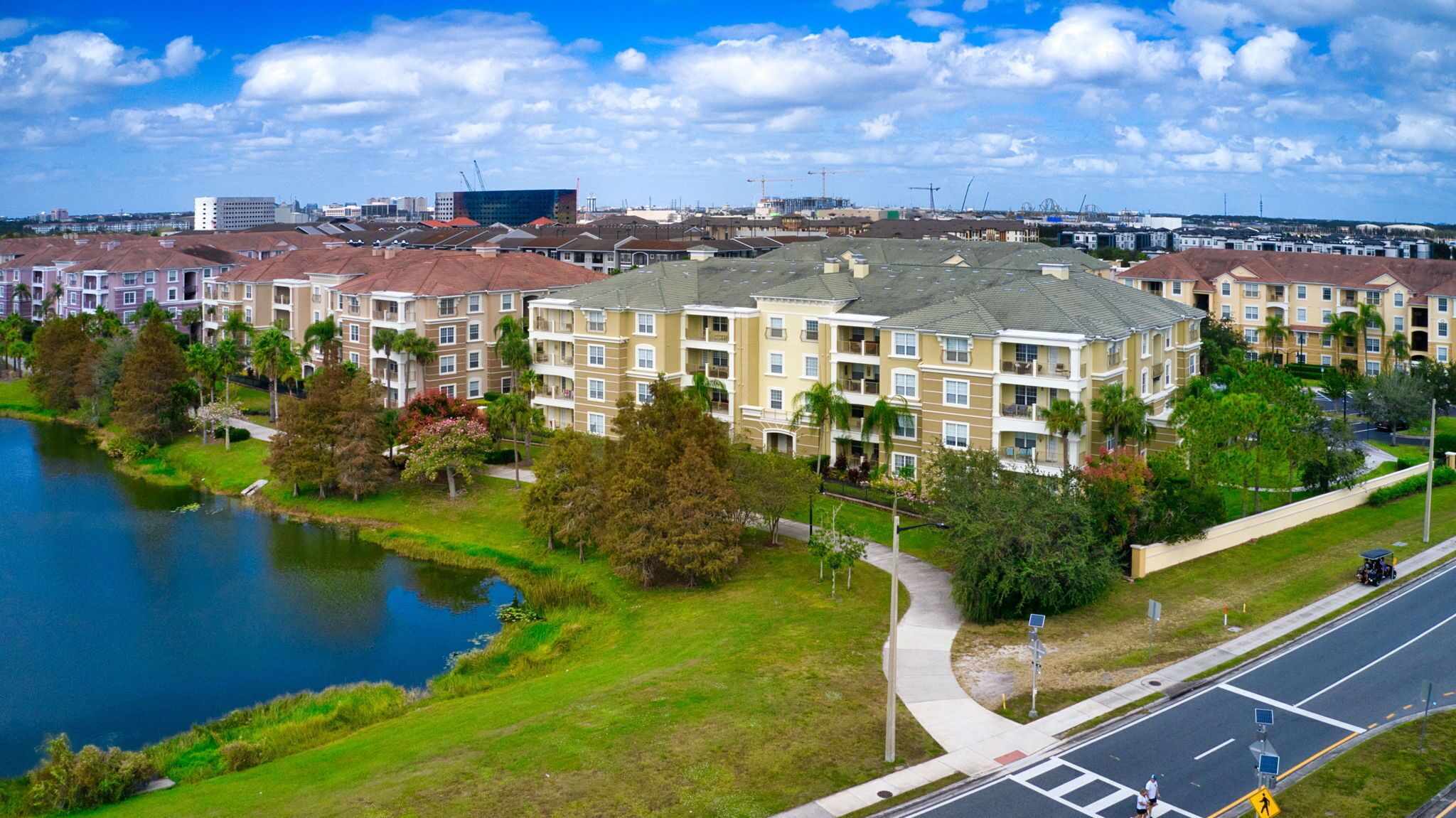 A residential building complex with multiple apartment buildings, a body of water, and a road with pedestrian crossings.