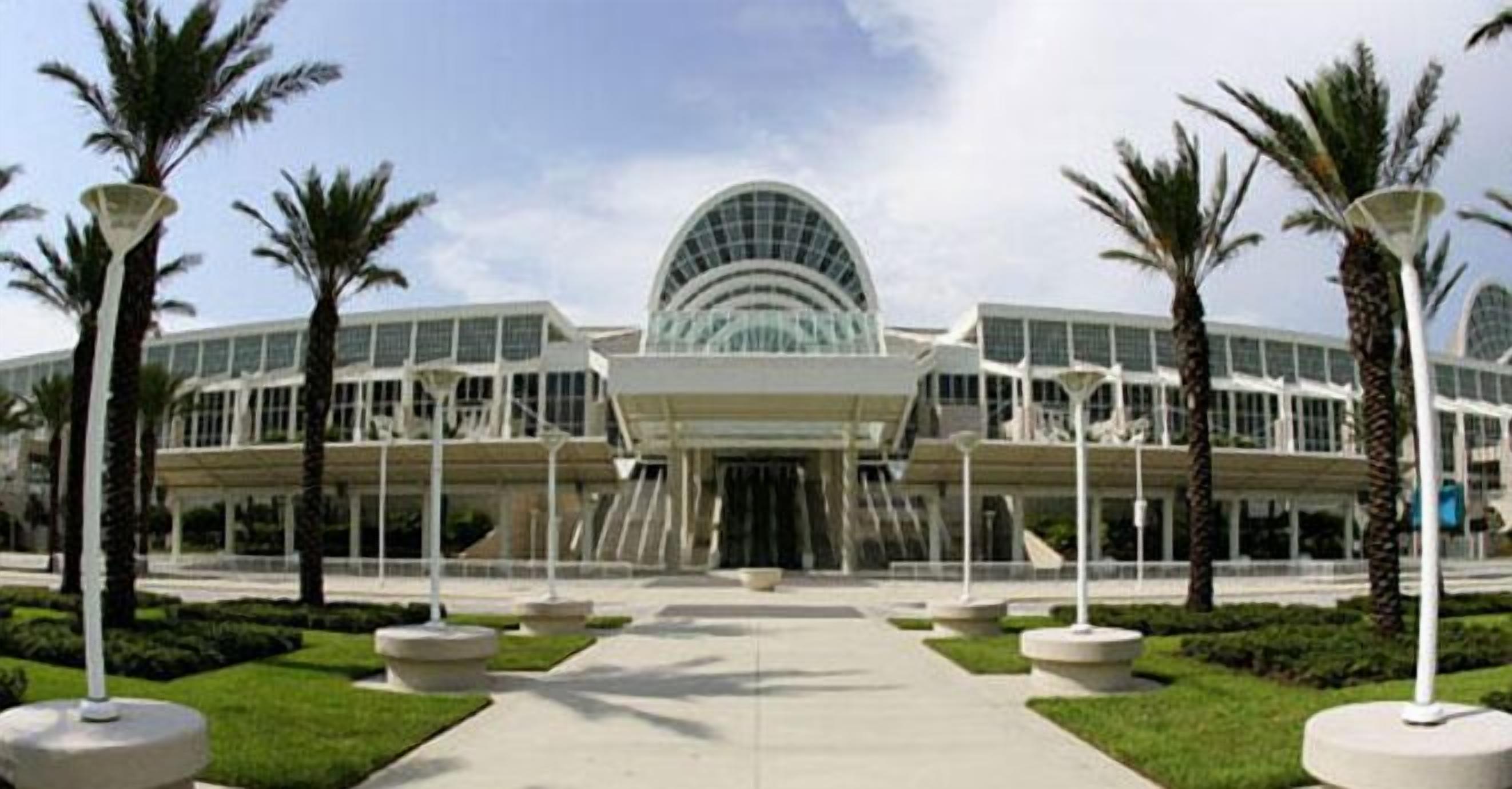 A modern building with a large glass dome entrance, surrounded by palm trees and a well-maintained lawn.