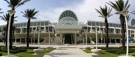 A modern building with a large glass dome entrance, surrounded by palm trees and a well-maintained lawn.