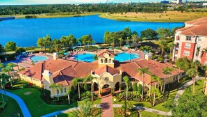 A resort with a central pool, a tennis court, and a large body of water in the background.