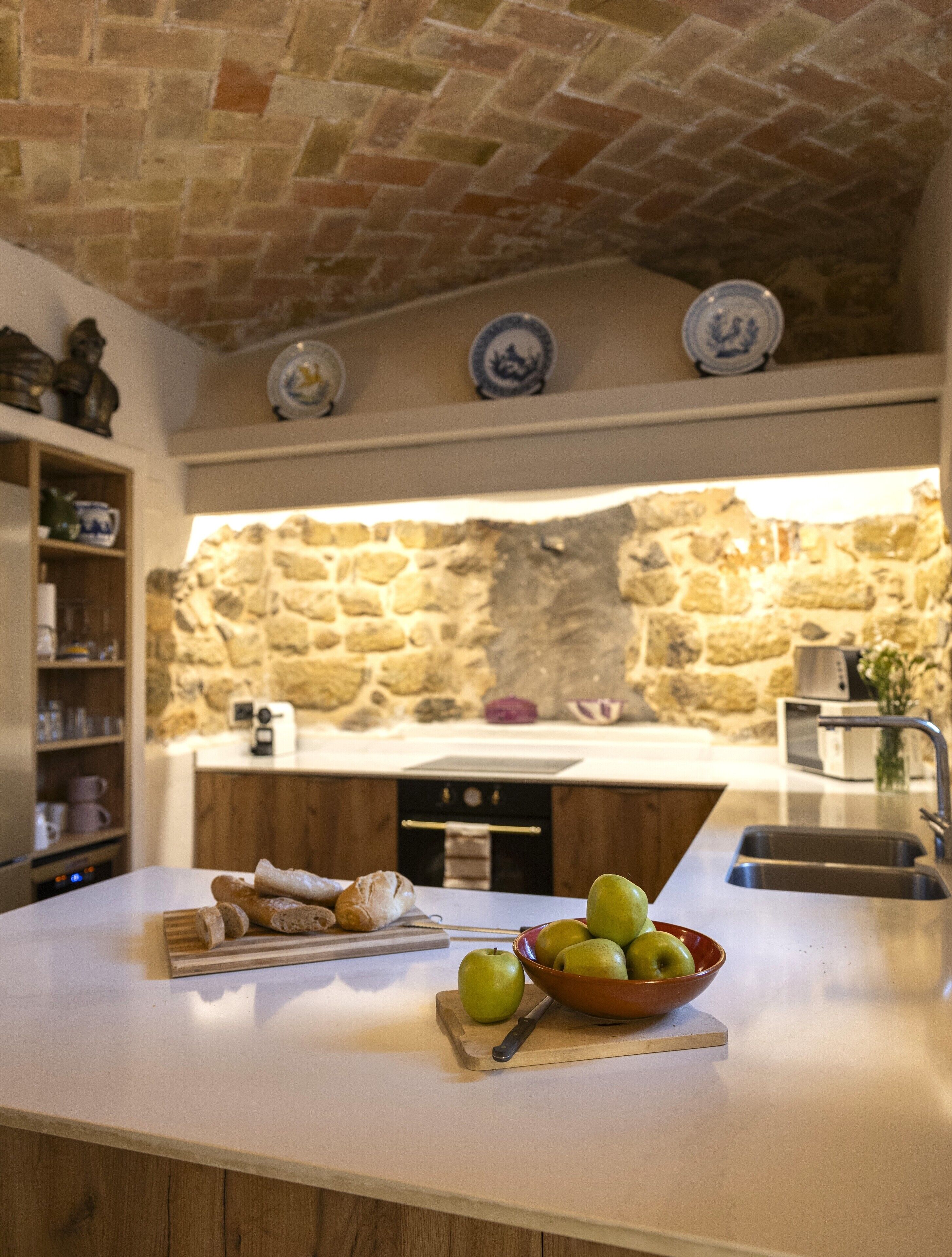 Une cuisine avec un mur en pierre, un plan de travail en bois et un saladier rempli de pommes.