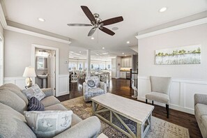 A spacious living room with a ceiling fan, a dining area, and a kitchen in the background.