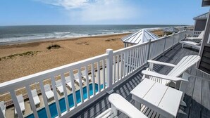 Een terras aan het strand met een zwembad, ligbedden en uitzicht op de oceaan.