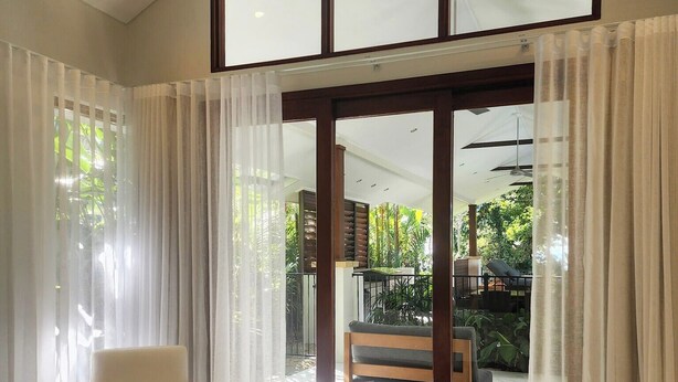 Un dormitorio con una cama grande, una silla y un ventanal corredero que da a un balcón con mobiliario exterior.