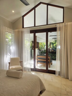 A bedroom with a large bed, a chair, and a sliding glass door leading to a balcony with outdoor furniture. - Pearl on Newell Beach 26 Rankin Street, Newell Beach QLD 4873 (Newell)