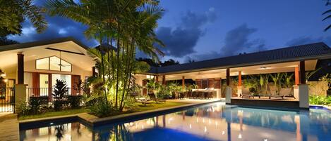 A modern house with a swimming pool, outdoor seating, and tropical plants.
