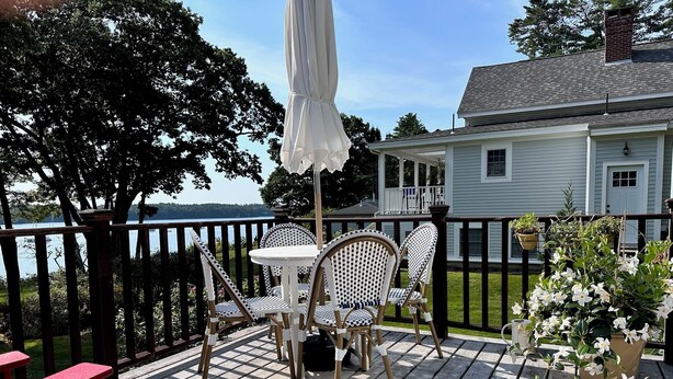 A wooden deck with a table and chairs, a red bench, and a white umbrella. - Full Moon on the Harraseeket, Freeport, Maine   (Freeport)