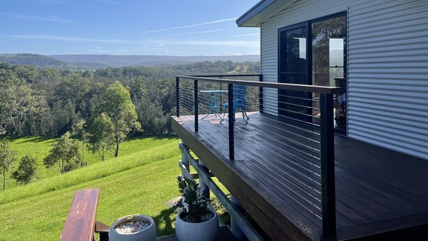 Et moderne hus med balkon med udsigt over et frodigt grønt landskab og fjerne bakker.
