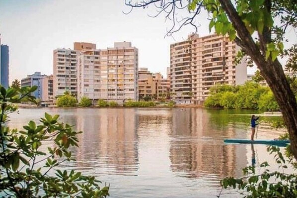 Vista de edifícios residenciais altos com um corpo d'água calmo em primeiro plano, refletindo os edifícios.