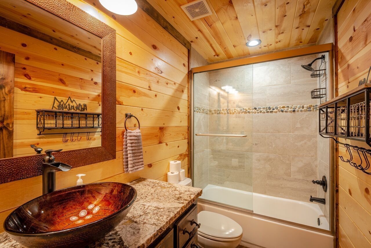 Een badkamer met houten inrichting, een douche met glazen wanden, een wastafel met een marmeren blad en een toilet.