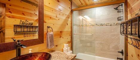 Een badkamer met houten inrichting, een douche met glazen wanden, een wastafel met een marmeren blad en een toilet.