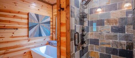 Baño de cabaña de madera con una bañera, ducha con baldosas de piedra y techo de madera.