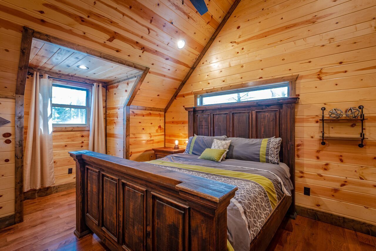 A wooden cabin bedroom with a large bed, wooden walls, and a sloped ceiling.
