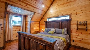 A wooden cabin bedroom with a large bed, wooden walls, and a sloped ceiling. - Luxury Broken Bow Cabin w/ Private Pond | Sleeps 18 (broken bow)