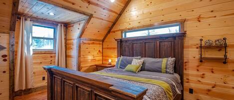 A wooden cabin bedroom with a large bed, wooden walls, and a sloped ceiling.