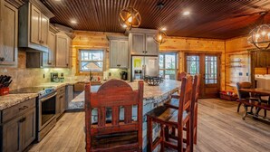 A spacious kitchen with granite countertops, wooden cabinets, and a central island with bar stools. - Luxury Broken Bow Cabin w/ Private Pond | Sleeps 18 (broken bow)