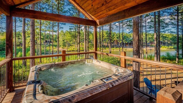 A wooden deck with a hot tub overlooking a lake and forest. - Luxury Broken Bow Cabin w/ Private Pond | Sleeps 18 (broken bow)