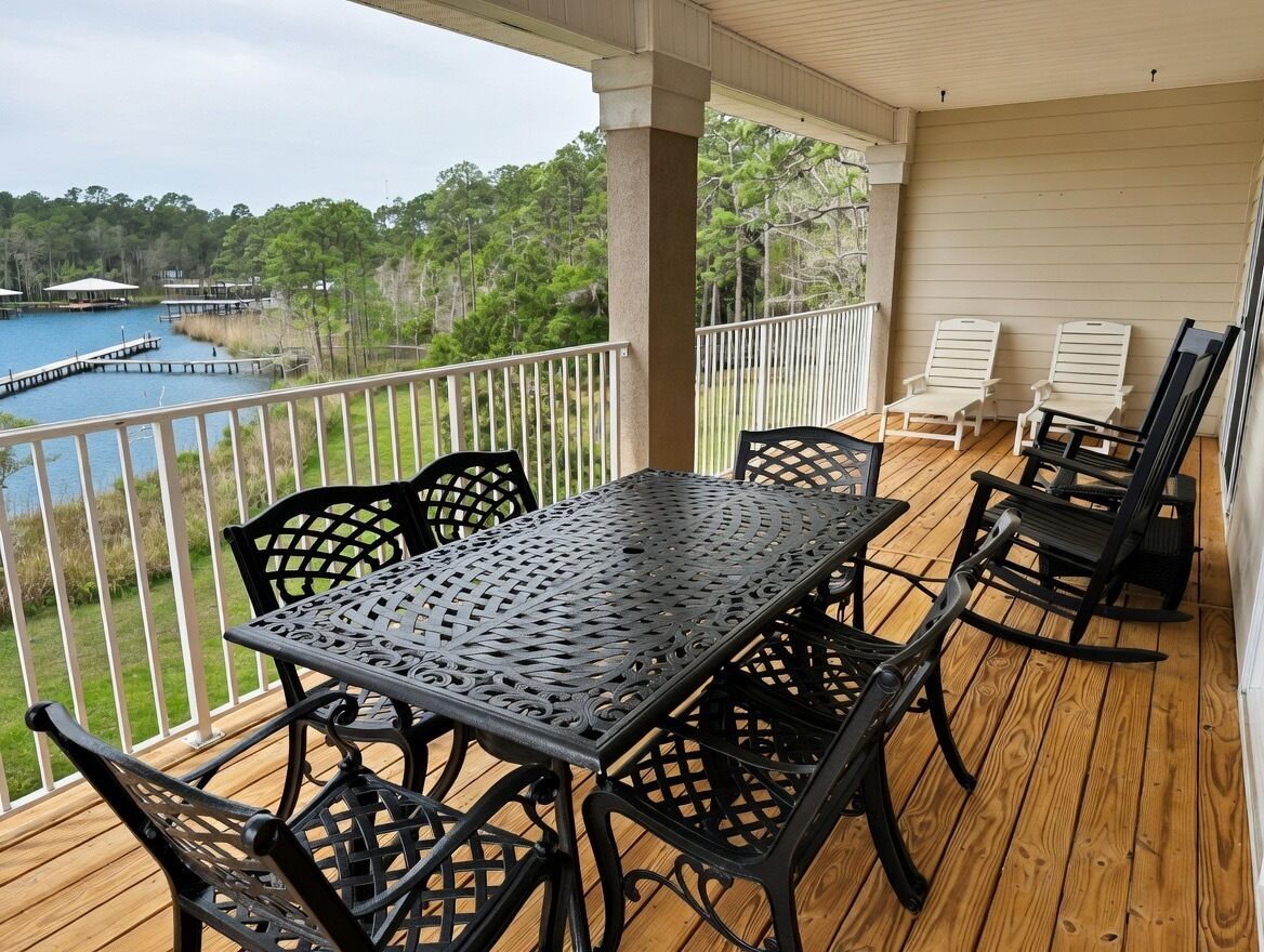 A covered outdoor deck with a table and chairs, overlooking a lake and dock.