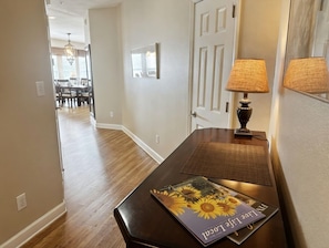 A hallway with a wooden floor, a door, a lamp, and a framed picture on the wall.
