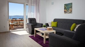 Ein Wohnzimmer mit grauem Sofa, einem Couchtisch und einem Essbereich mit Tisch und Stühlen.
