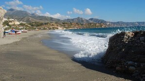 A beach with boats, rocky terrain, and mountains in the background.