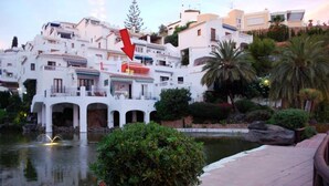 A white building with balconies, a water feature, and a pathway.
