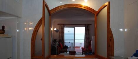 A living area with a view of the sea, a balcony, and a wooden archway.