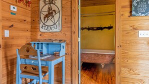 Une pièce rustique en bois, avec un bureau bleu, une enseigne représentant un rodéo du Texas et une baignoire.