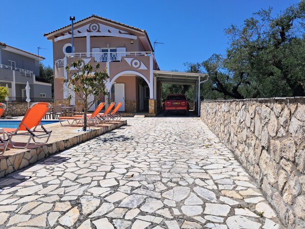 A pool area with stone flooring, orange lounge chairs, and a building with a tiled roof and balconies. - Beautiful Villa Ella with private pool.  E.O.T Licence MHTE 0428K9200476001 (Zakynthos (Zante))