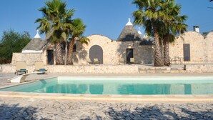 Zona de piscina con paredes de piedra y palmeras.