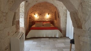 Habitación con paredes de piedra, una cama, dos luces fijadas a la pared y un radiador.