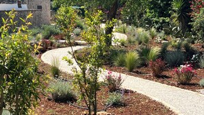 Un jardín con un sendero sinuoso, diversas plantas y un edificio de piedra con techo cónico.