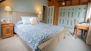 Quarto com cama, cabeceira de madeira, mesas de cabeceira, um criado-mudo, uma cadeira e um guarda-roupa com portas.