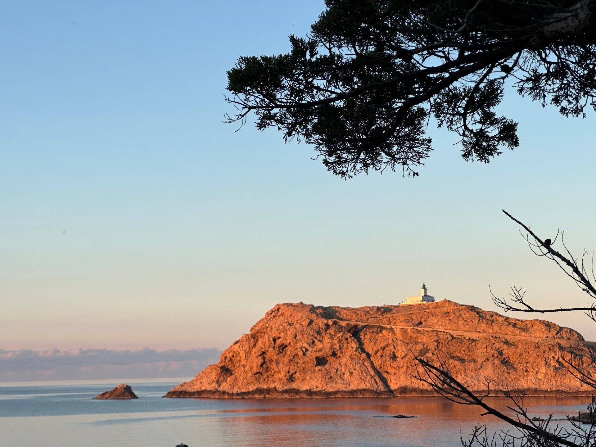 Une île rocheuse surmontée d’un phare, entourée d’eaux calmes et baignée d’un ciel dégagé.