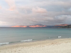 A beach with clear water, a sandy shore, and distant mountains under a cloudy sky. - Exceptional sea view! Apartment facing the sea, central Rousse Island (L'île-Rousse)